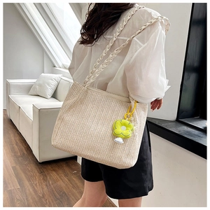 Detail of beige woven tote bag with braided handles and yellow flower charm