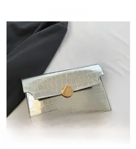 Detail of silver crocodile pattern envelope clutch featuring a large gold metal buckle