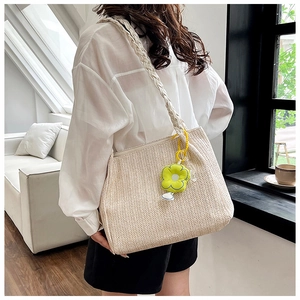 Chic off-white woven tote bag with green floral charm shown on a stylish model