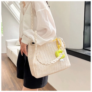 Detail of cream woven tote bag with large capacity and floral charm on shoulder