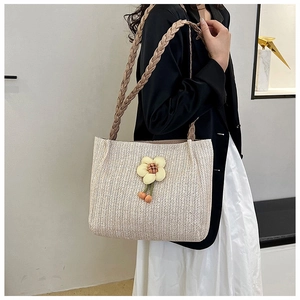 Detail view of cream woven tote bag with a small yellow flower charm on model's shoulder
