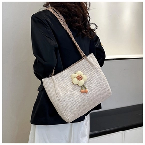 Detail of woven straw tote bag with floral accents and cherry charms on a model
