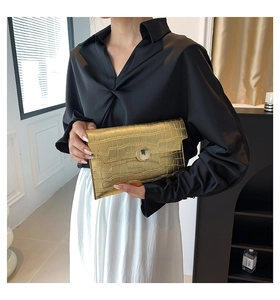 Pochette dorata a rilievo coccodrillo con chiusura in metallo su sfondo camicia nera