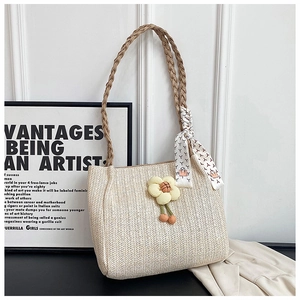 Detailed view of woven straw shoulder bag with floral charm and decorative silk scarf