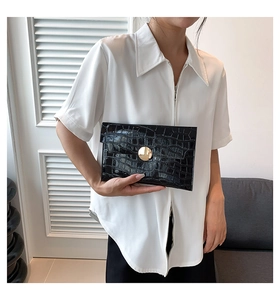 Modella tiene una pochette nera con motivo a coccodrillo e fibbia tonda dorata