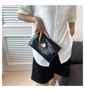 Close-up of black crocodile pattern patent leather handbag with gold metal clasp detail