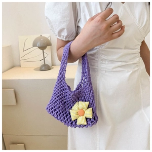 Detail of purple woven handbag with a large floral charm held by a model in white dress