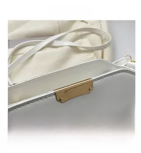 Close-up of white crossbody bag featuring a trapezoidal gold metal decorative accent