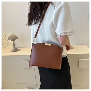 Detail view of brown minimalist shoulder bag with wavy top edge and gold metal trim