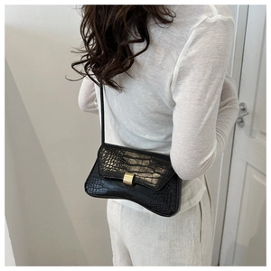 Detail of black crocodile texture shoulder bag with gold clasp and curved bottom