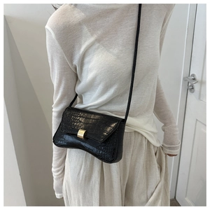 Close-up of black crocodile embossed shoulder bag with gold clasp on a model outfit