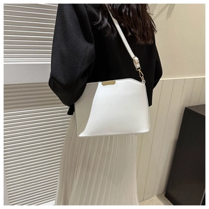 Detailed view of white crossbody bag with gold metal clasp on a model in soft lighting
