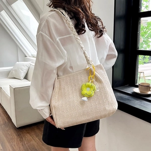 Vintage beige straw shoulder bag with green flower charm in a minimalist setting