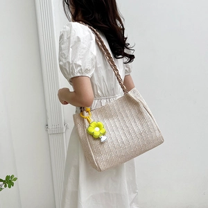 Chic cream woven straw tote bag with brown braided straps and a yellow flower pendant