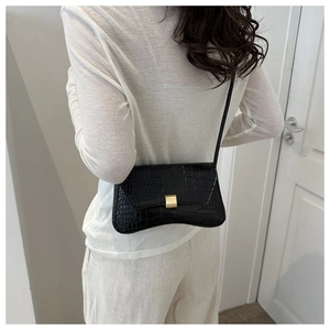Detail of black crocodile texture crossbody bag with gold buckle on a model shoulder