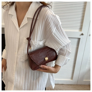 Detail of burgundy crocodile-embossed leather crossbody bag with gold rectangular clasp