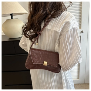 Detail of dark brown crocodile texture baguette bag with knotted strap and gold buckle
