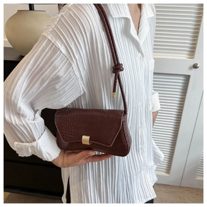 Detail of burgundy crocodile pattern leather bag with golden buckle and strap knot
