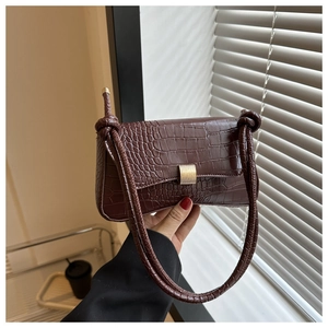 Detail of dark brown crocodile pattern baguette bag with golden metal buckle and knot strap