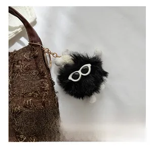 Gros plan d'une breloque en peluche noire avec lunettes sur un sac seau en tweed