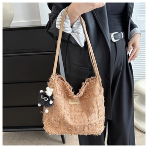 Détail d'un sac seau kaki texturé avec motif à franges et accessoire en peluche agneau