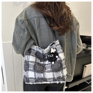 Détail du cabas à carreaux avec bords effilochés et breloque pelucheuse sur mannequin