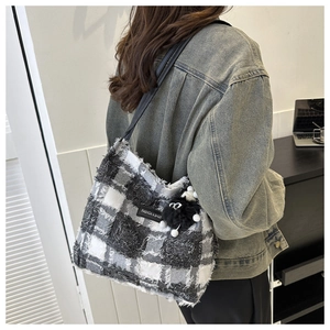 Détail d'un sac cabas à carreaux avec bords frangés et pompon en peluche sur un modèle