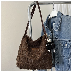 Sac fourre-tout marron texturé avec franges et breloque monstre poilue sur un cintre
