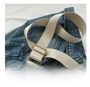Dettaglio della tracolla in nylon intrecciato crema con fibbie in metallo dorato su denim