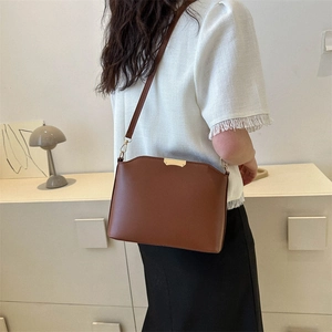Minimalist dark brown crossbody bag with gold buckle in a modern lifestyle setting