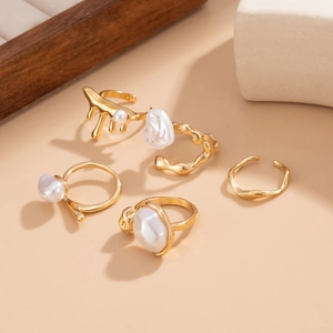 Detail of five-piece gold ring set featuring irregular baroque pearls on beige background