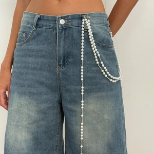 Detail of faux pearl layered waist chain with star tassel on blue wide-leg denim jeans