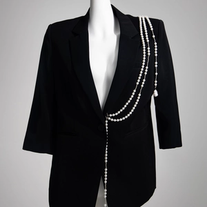 Détail de la chaîne d'épaule en perles multicouches et broche étoile sur un blazer noir