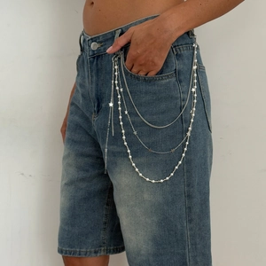 Detail of layered silver metal waist chain with white pearls and star charms on denim