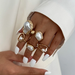 Detail of hand wearing gold irregular rings set with baroque pearls and hollow geometric designs