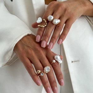 Detail of baroque pearl ring set with irregular gold bands and sparkling stones on finger