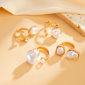 Detail of four gold baroque pearl open rings set on neutral textured stone and silk