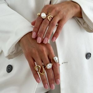 Detailed view of layered gold rings with baroque pearls on a model wearing white