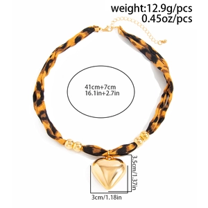 Macro view of leopard print fabric choker with large gold heart pendant and sizing details