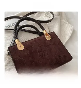 Detail of embossed clover pattern and woven leather handle on dark brown crossbody bag