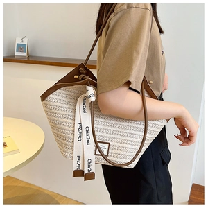 Detail of straw tote bag with brown leather trim and decorative graphic strap