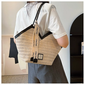 Detail view of woven straw tote bag with black contrast trim and stylish lettered strap