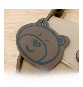 Detail of a brown leather bear charm with gold chain on a stylish square crossbody bag