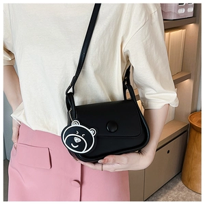 Detail showing a black round-bottom shoulder bag with a cute bear pendant on a model
