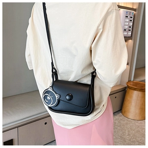 Detail of black saddle bag with asymmetrical flap and cute bear charm worn by a model
