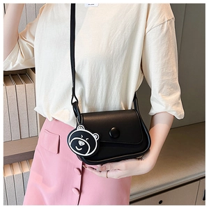 Detail view of black leather saddle bag with round buckle and cartoon bear charm