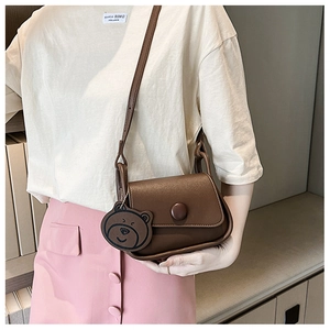 Detail of dark brown matte leather saddle bag with a cute bear charm on a model
