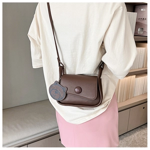 Rear view of model wearing minimalist brown crossbody bag with blue bear charm