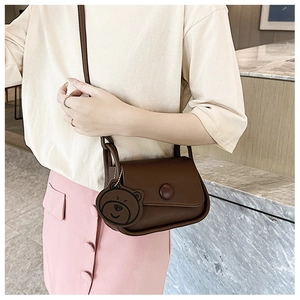 Detail of dark brown leather crossbody bag with round buckle and cute bear charm accessory