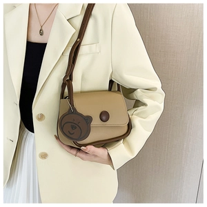 Detail of khaki square crossbody bag with brown bear charm and round decorative buckle